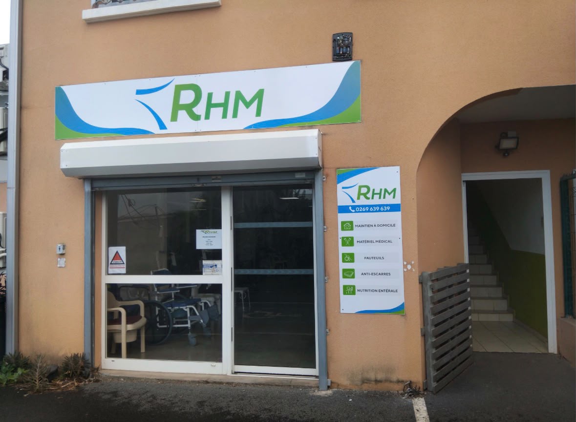 Façade d’un local RHM avec enseigne verte et bleue, vitrine ouverte et panneau d’informations médicales.